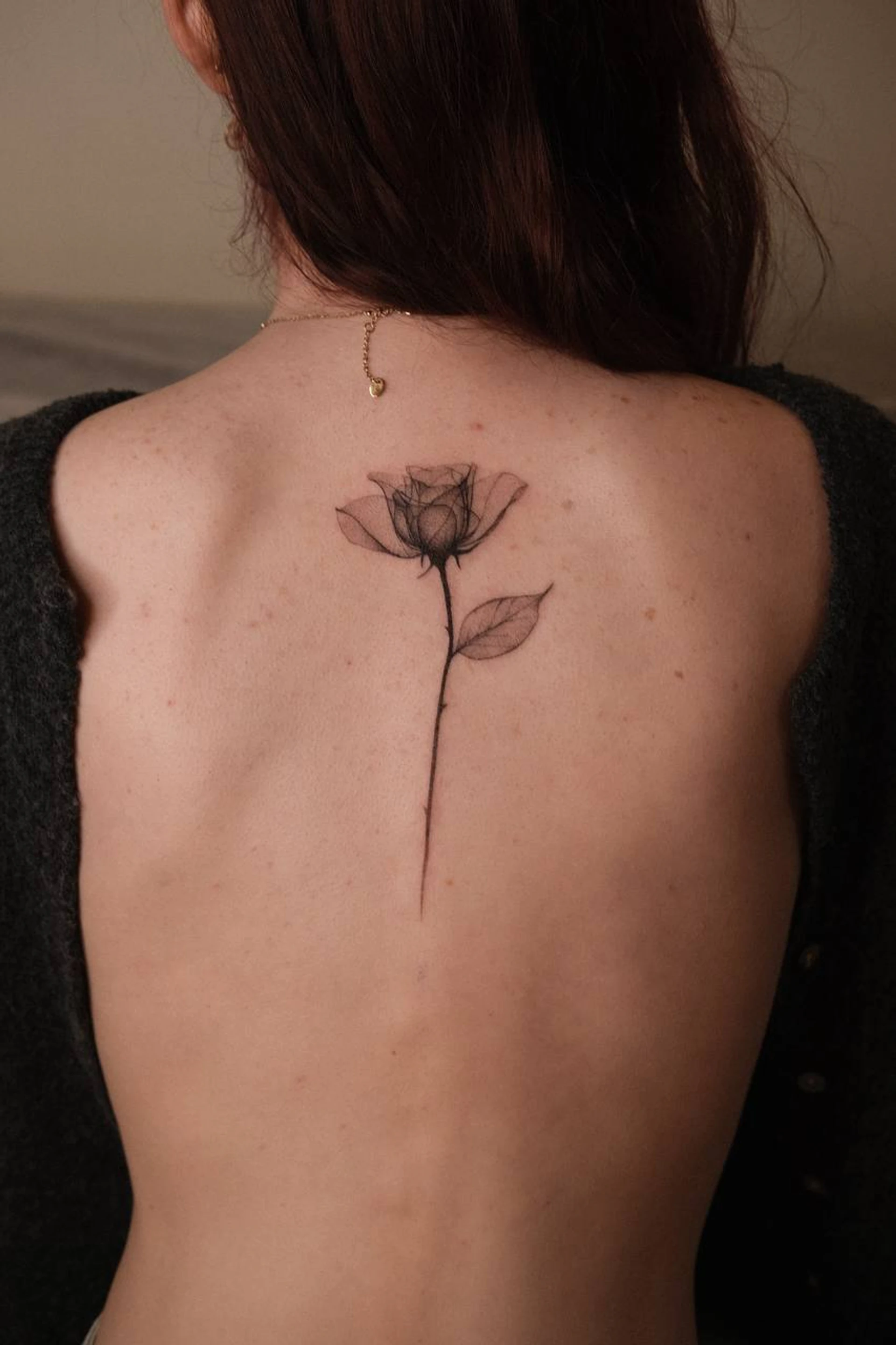 Fine-line rose handpoke tattoo on the upper back by Maria Pokes